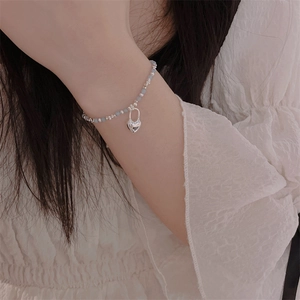 Detail of beaded bracelet with light blue beads and a polished silver heart charm pendant