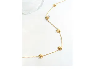 Detailed view of the gold-plated daisy pendant necklace on an artistic book background