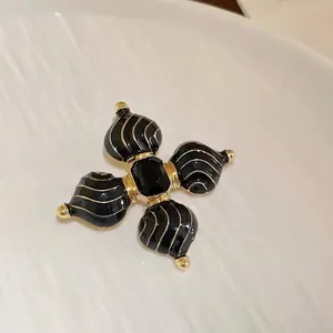 Makroaufnahme einer Retro-Kreuzbrosche mit schwarzer Emaille und Edelsteinverzierungen