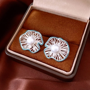 Detailed shot of silver hollow flower earrings with teal enamel and pearls on velvet