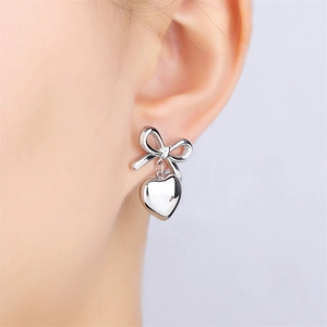 Close-up of silver bow and heart pendant earring worn by a model in a high-quality shot