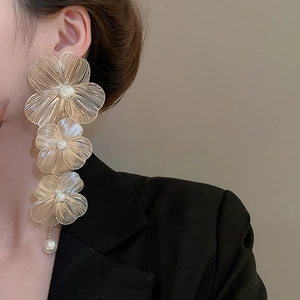 Dettaglio di orecchini a fiore dorati con petali in metallo e perle su una modella