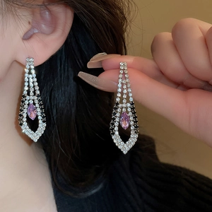 Macro shot of drop earrings featuring purple gemstone and rhinestones on a female model