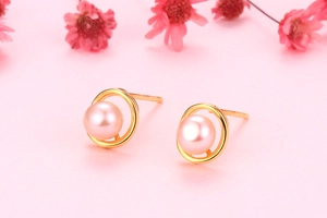 Close-up of minimalist gold ring earrings with small pink freshwater pearls on pink background