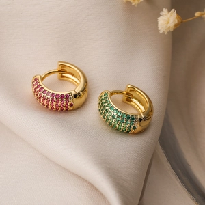 Detail of gold-plated hoop earrings with pink and green zircon on beige silk fabric