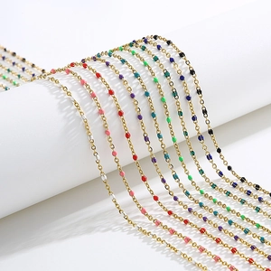 Golden mask chains with colorful enamel beads displayed on minimalist white props