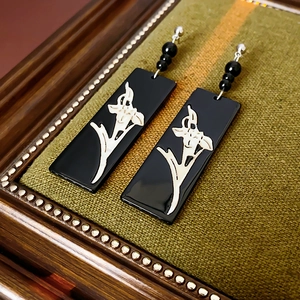 Close-up of geometric earrings with white floral inlay on black rectangular pendants