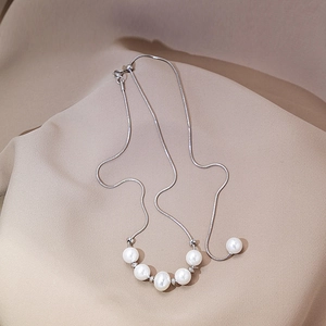 Detailed view of white pearls aligned on a silver snake chain necklace with beige backdrop