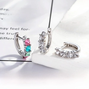 Close-up of 3mm zircon earring settings with hand-set colorful gemstones on stone surface
