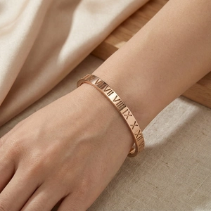 Gros plan d'un bracelet en acier titane or rose avec des chiffres romains gravés