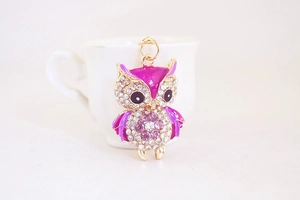 Detail of owl keychain with purple rhinestones and enamel on golden metal base