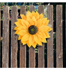 Detailed view of yellow burlap sunflower wreath hanging on a rustic wooden garden fence