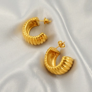 Fashionable gold C-shaped stainless steel earrings with a ribbed texture on grey silk