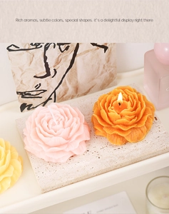 Close-up of lit orange rose and pink peony flower candles on beige stone display