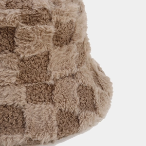 Dettaglio ravvicinato del motivo a scacchi in peluche marrone e beige sul cappello invernale