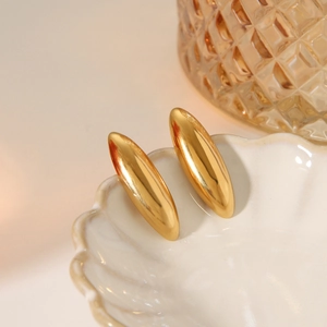 Macro shot of polished gold oval earrings resting on a white shell plate