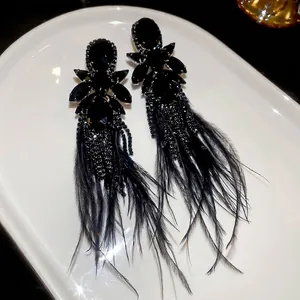 Dark style long tassel earrings with black feathers and rhinestones on white plate