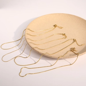 Detailed view of four golden snake bone chains with lobster clasps on a beige tray