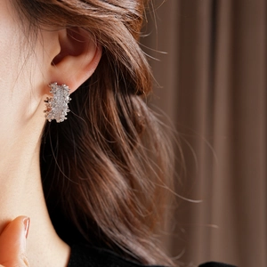 Close-up of silver C-shaped earrings with irregular lava texture on female model