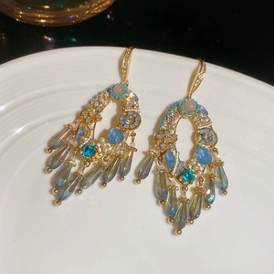 Dettaglio di orecchini dorati con nappe e cristalli di zircone blu su porcellana bianca