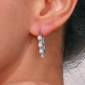 Macro shot of silver U-shaped earrings featuring four elegant white round pearls