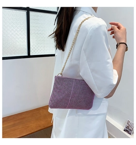 Detail of pink rhinestone shoulder bag with gold chain strap on white blazer