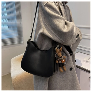 Detail view of black textured shoulder bag with a brown rabbit plush charm on strap