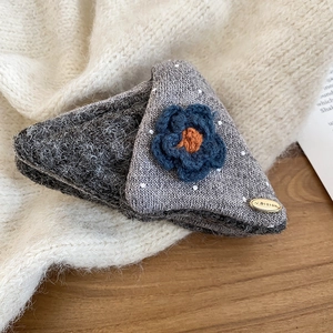 Close-up of handmade knit flower hair claw clip with gold tag on a warm knit sweater