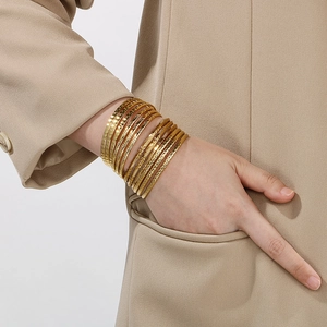 Detail of stacked gold stainless steel bangles with diverse textures on a model wrist