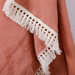Close-up of reddish-brown muslin baby swaddle fabric with off-white fringe tassels