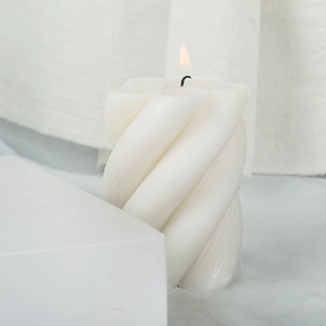 Lit white spiral pillar candle with vertical texture on minimalist white background