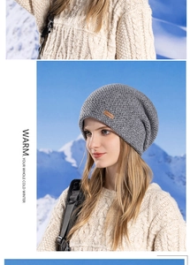Détail du bonnet en tricot gris avec étiquette en cuir devant un paysage de montagne enneigée