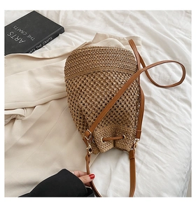 Close-up of brown straw bucket bag with leather strap on white linen with a book