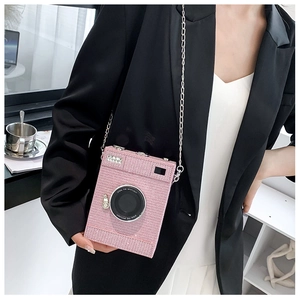 Pink glitter camera-shaped crossbody bag with a silver metal chain strap on a model