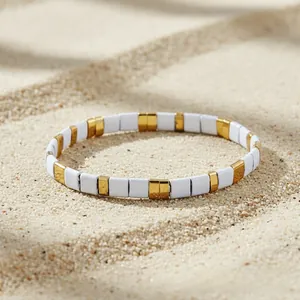 Detail of bohemian beach bracelet with white and gold tiles on soft sea sand