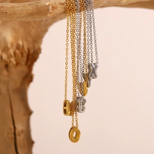 Gros plan de colliers avec pendentifs lettres creuses en or et argent sur une branche