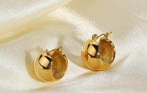 Macro view of polished 18K gold plated spherical stud earrings on silk fabric background