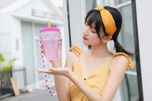 Detailed view of pink watermelon-shaped plastic cup with straw and patterned shoulder strap