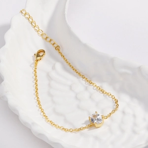 Detailed close-up of a gold-plated bracelet with a clear zircon on a white ceramic tray