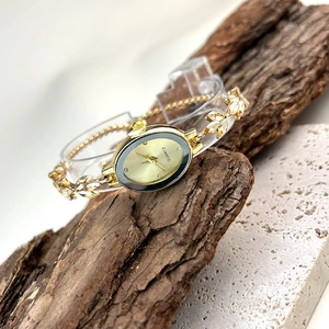 Macro detail of oval gold watch dial and decorative leaf-shaped metal strap links