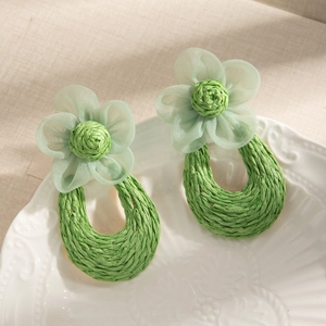 Detail of mint green mesh flower earrings with artisanal woven raffia ring pendant