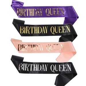 Detail showing satin birthday queen sashes in purple, black, and pink with metallic text