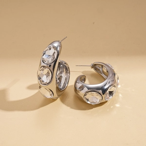 Detail of silver C-shaped hoop earrings featuring three large sparkling round gemstones
