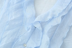 Detail of light blue sleeveless top with ruffled V-neck and delicate shell button
