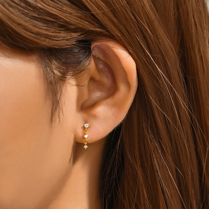 Detail of golden fringe stud earring with four vertical zircons on model ear