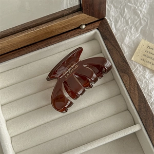 Detail of amber brown oval hair claw clip with gold label on white velvet tray