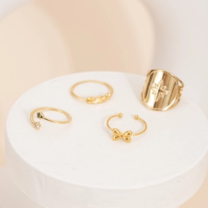 Set of four gold stainless steel rings featuring star, bow, and heart designs on a stand