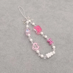 Close-up of pink beaded phone charm with bow, heart, and bear pendant on grey background