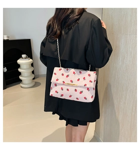 Fashionable strawberry print shoulder bag with gold chain strap shown on model's shoulder