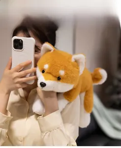 Close-up of soft brown and white plush Shiba Inu toy held by a model in a cozy setting